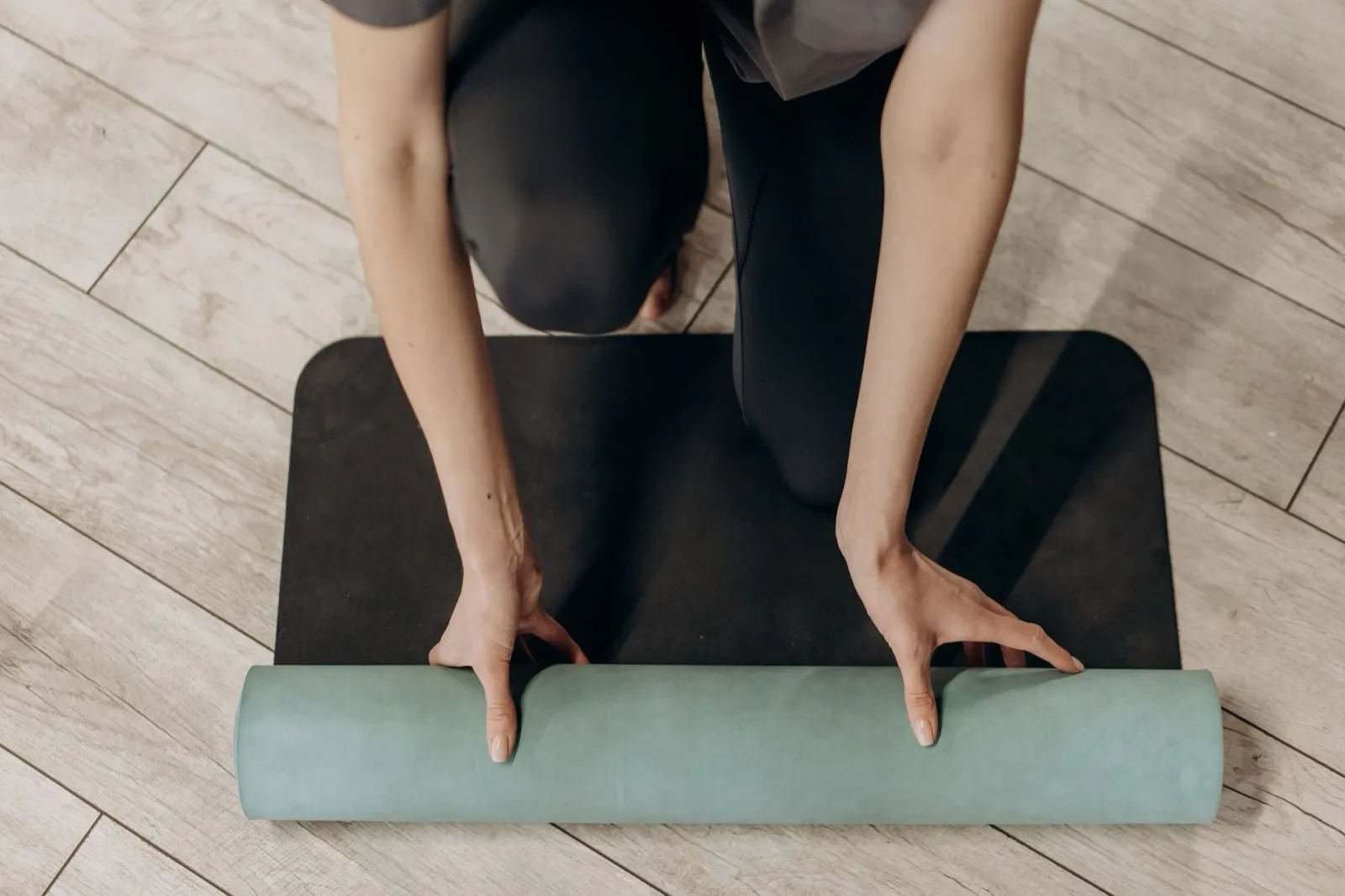 Hands unrolling an exercise mat on a wooden floor at home