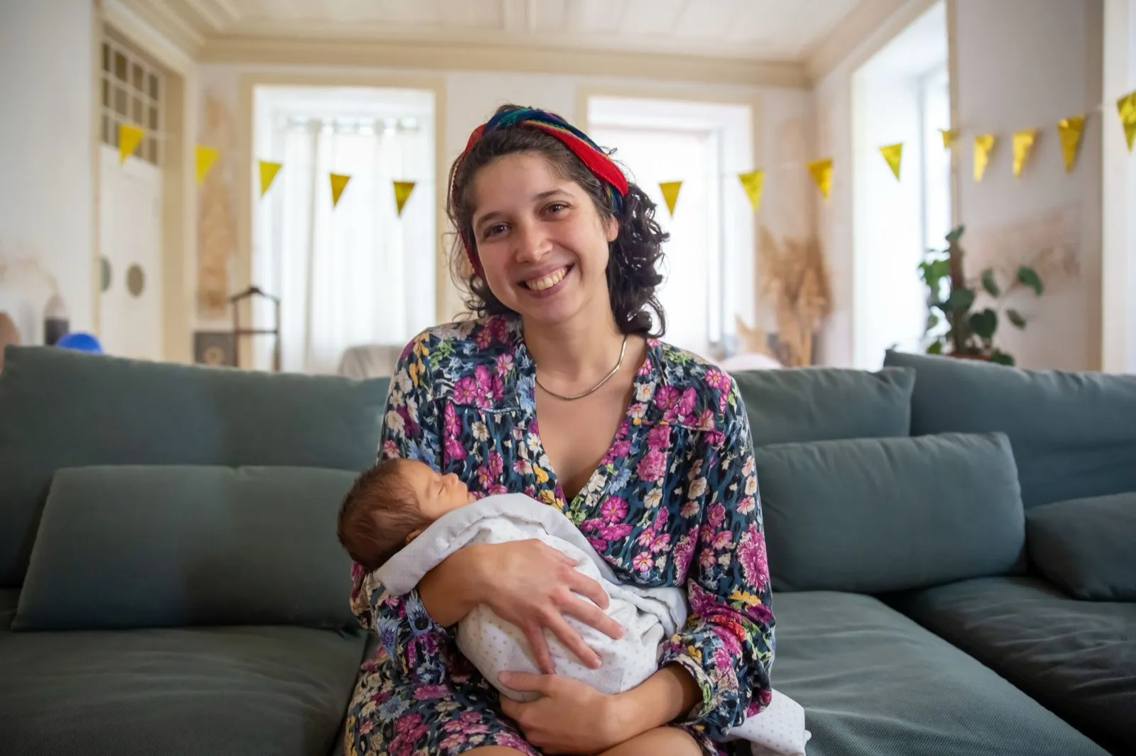 A parent sitting at home holding a sleeping newborn